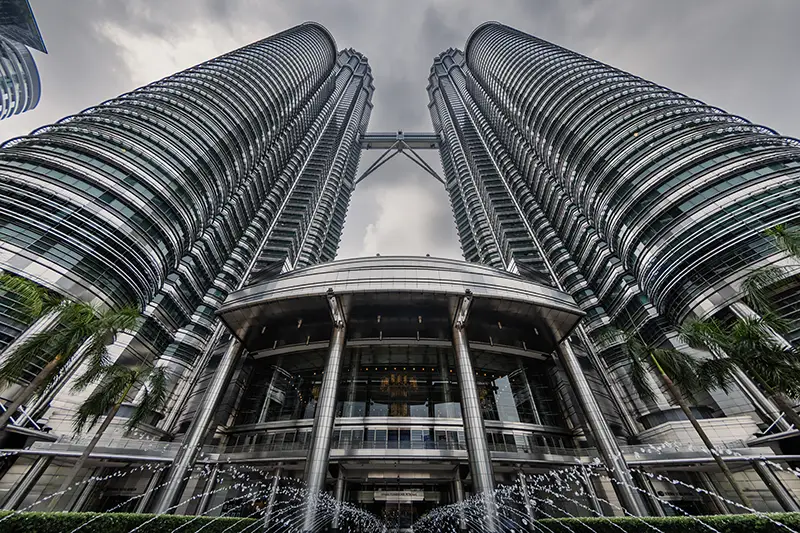 Low-angle view of the iconic Petronas Twin Towers in Kuala Lumpur with a dramatic sky and fountain — a top highlight and ideal starting point for your Kuala Lumpur 2 days itinerary.