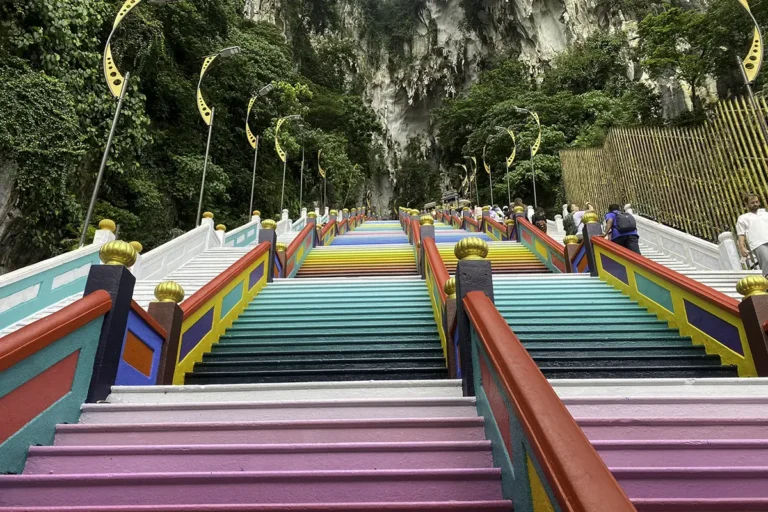 Colorful staircase leading up to the temple cave at Batu Caves, Malaysia, surrounded by lush greenery and limestone cliffs.